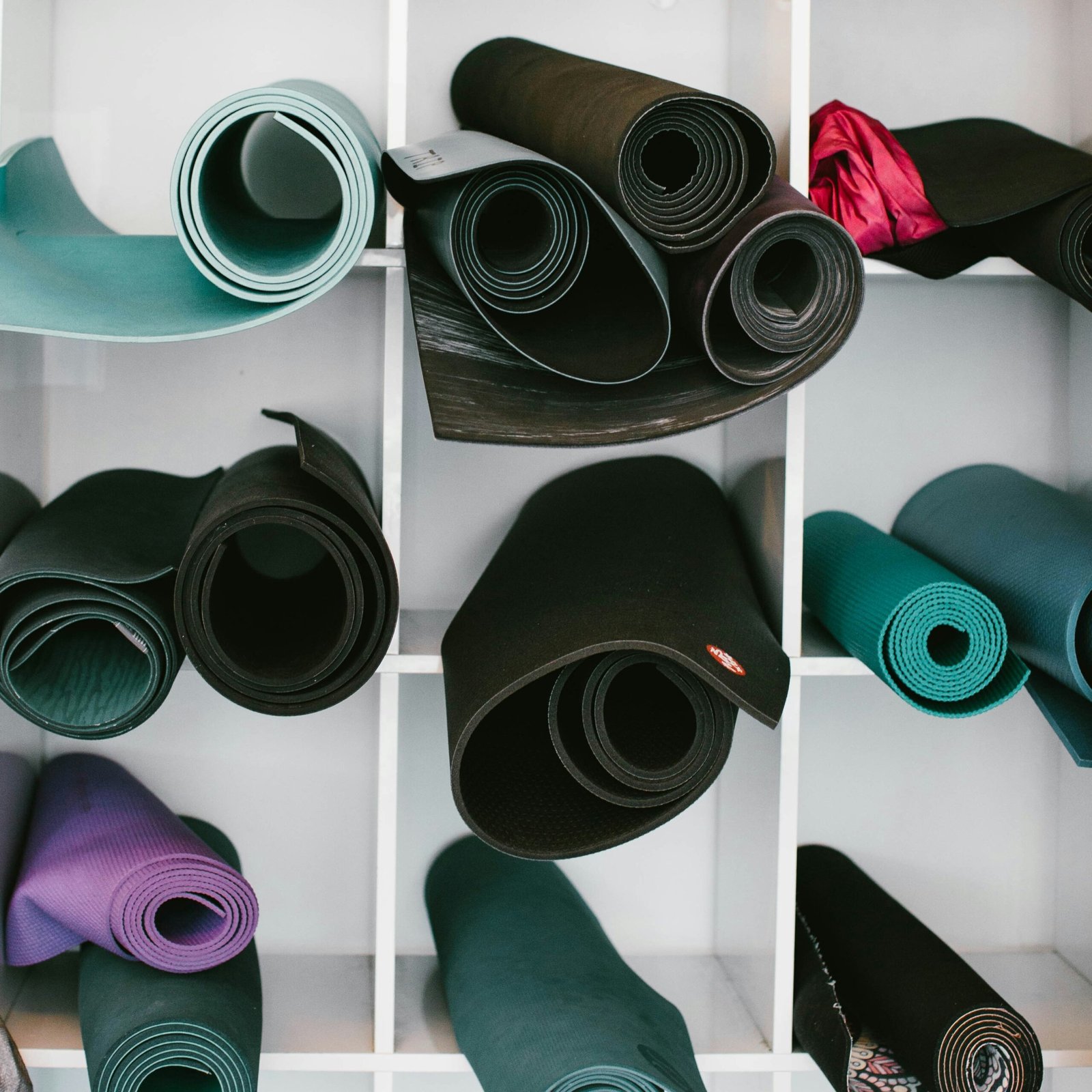 Rolled-up yoga mats in different colors, including black, teal, purple, and pink, neatly stored in shelf